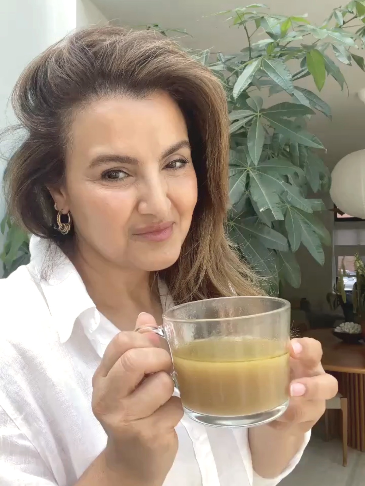 a glass cup of golden bone broth, held in both hands