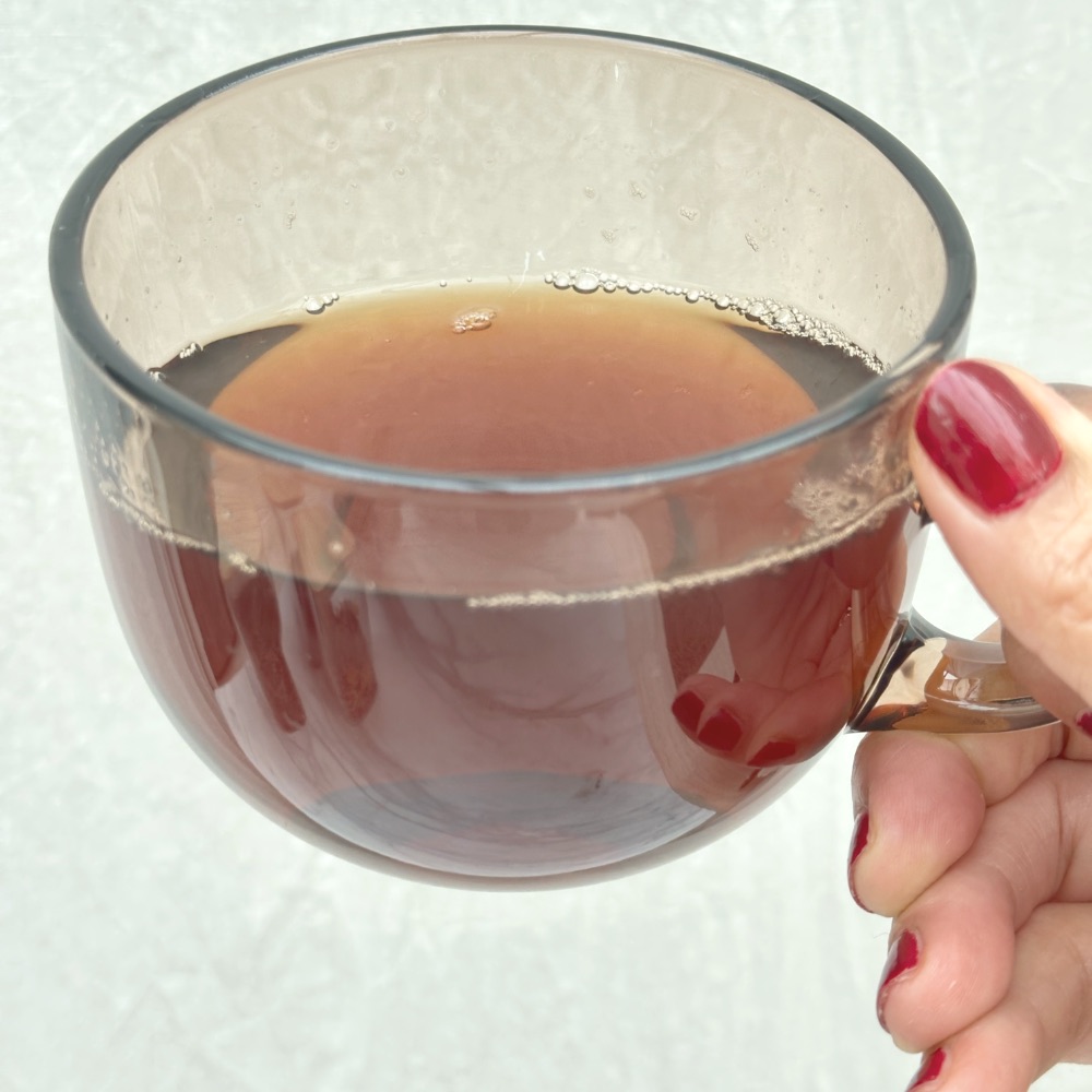 a hand holding a glass cup of nettle, dandelion and mint mineral tea