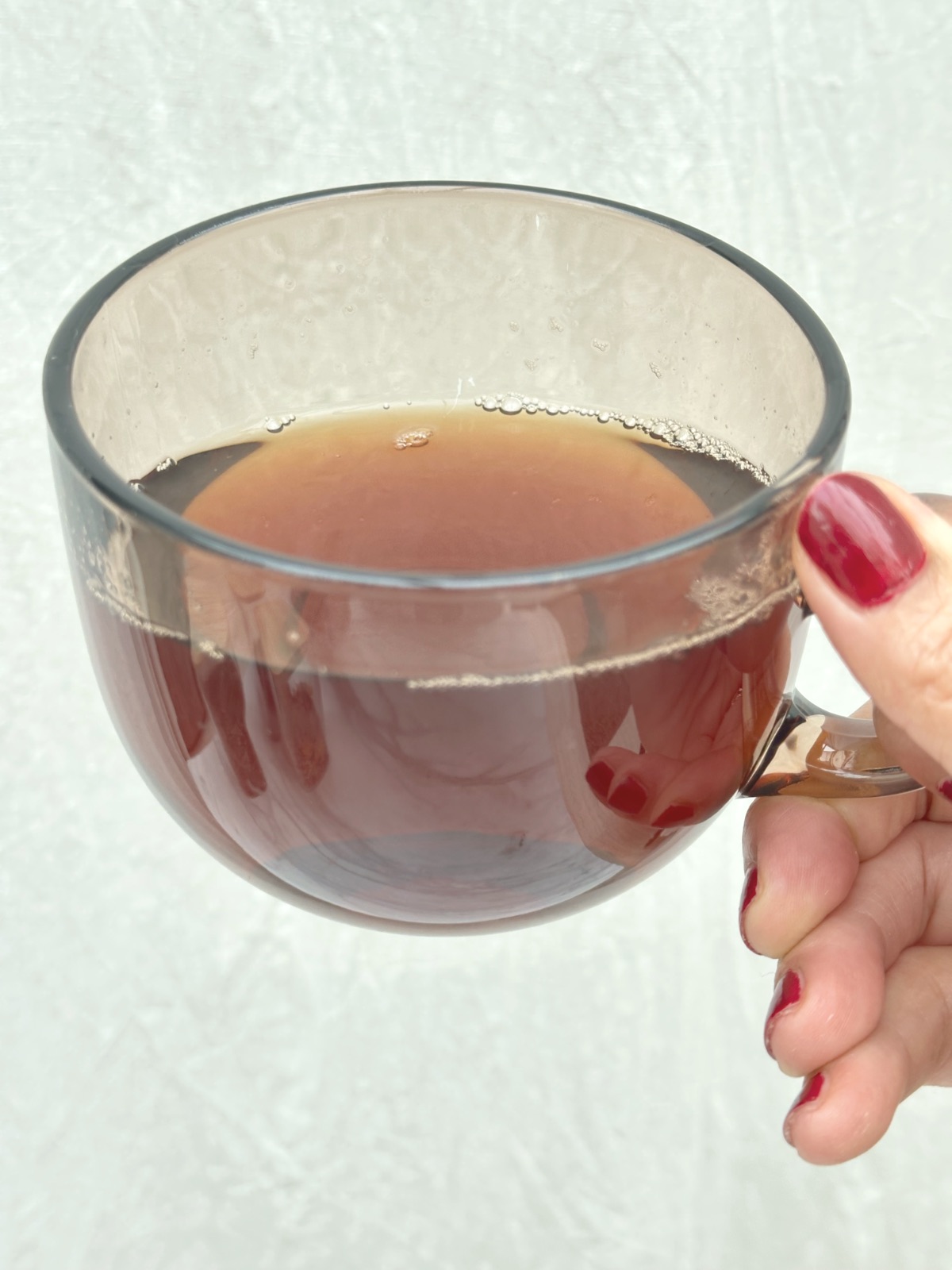 a hand holding a glass cup of the finished tea, dark amber going to red brown