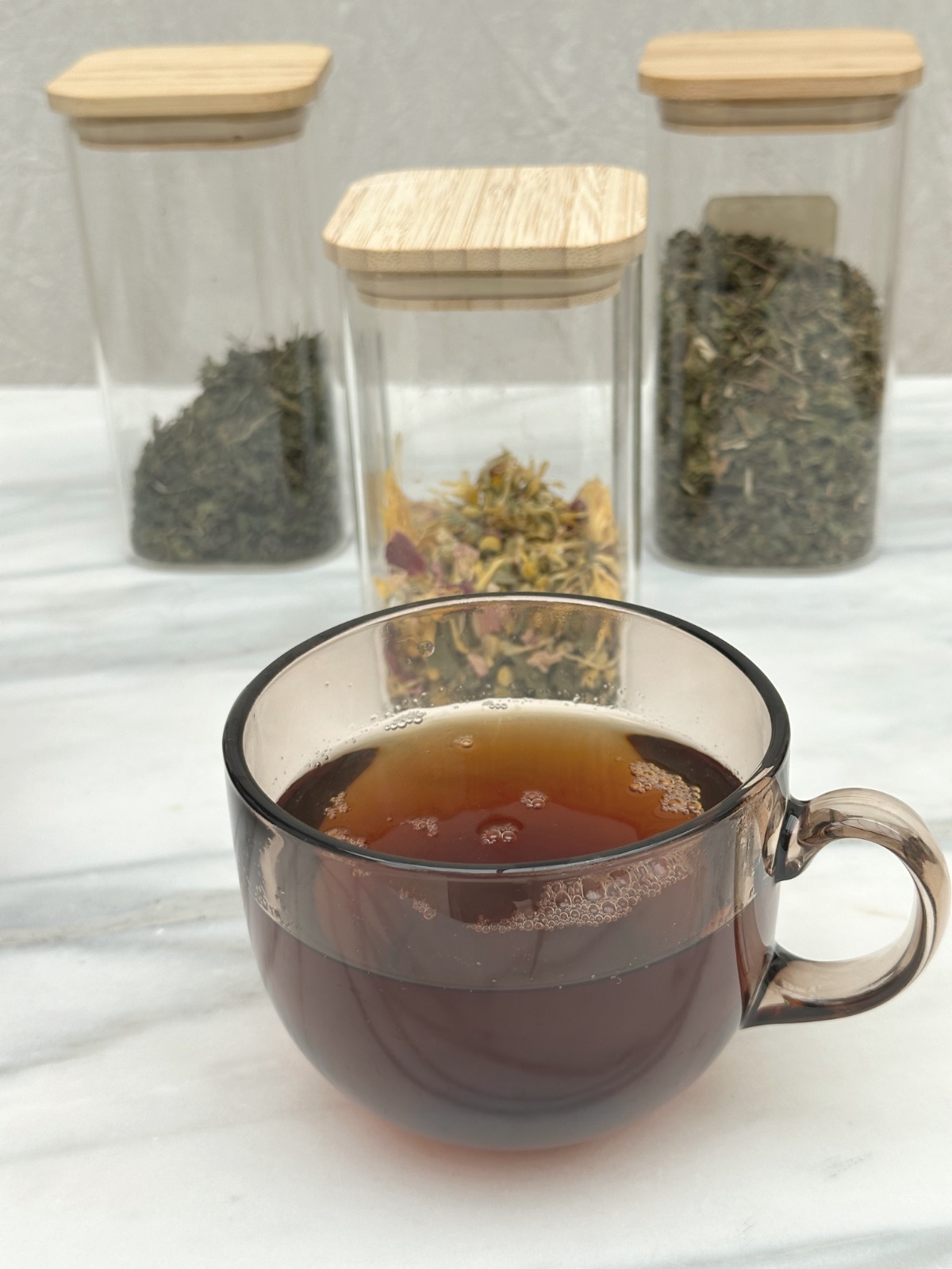 a cup of the tea in front of the glass jars the dried herbs are kept in